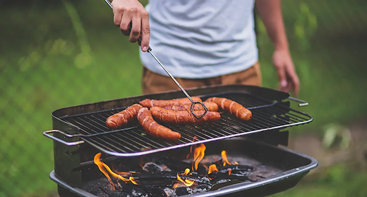 Image of sausages being grilled on a barbecue over an open flame outdoors
