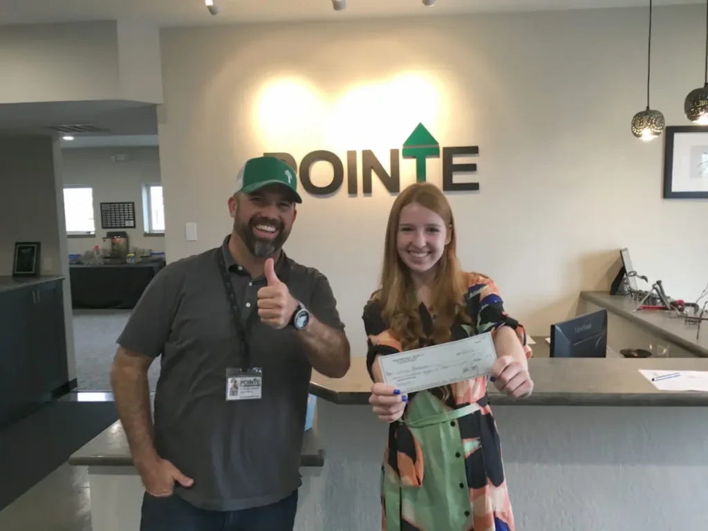 Image of a woman holding a check with a staff member inside a Pointe office reception area