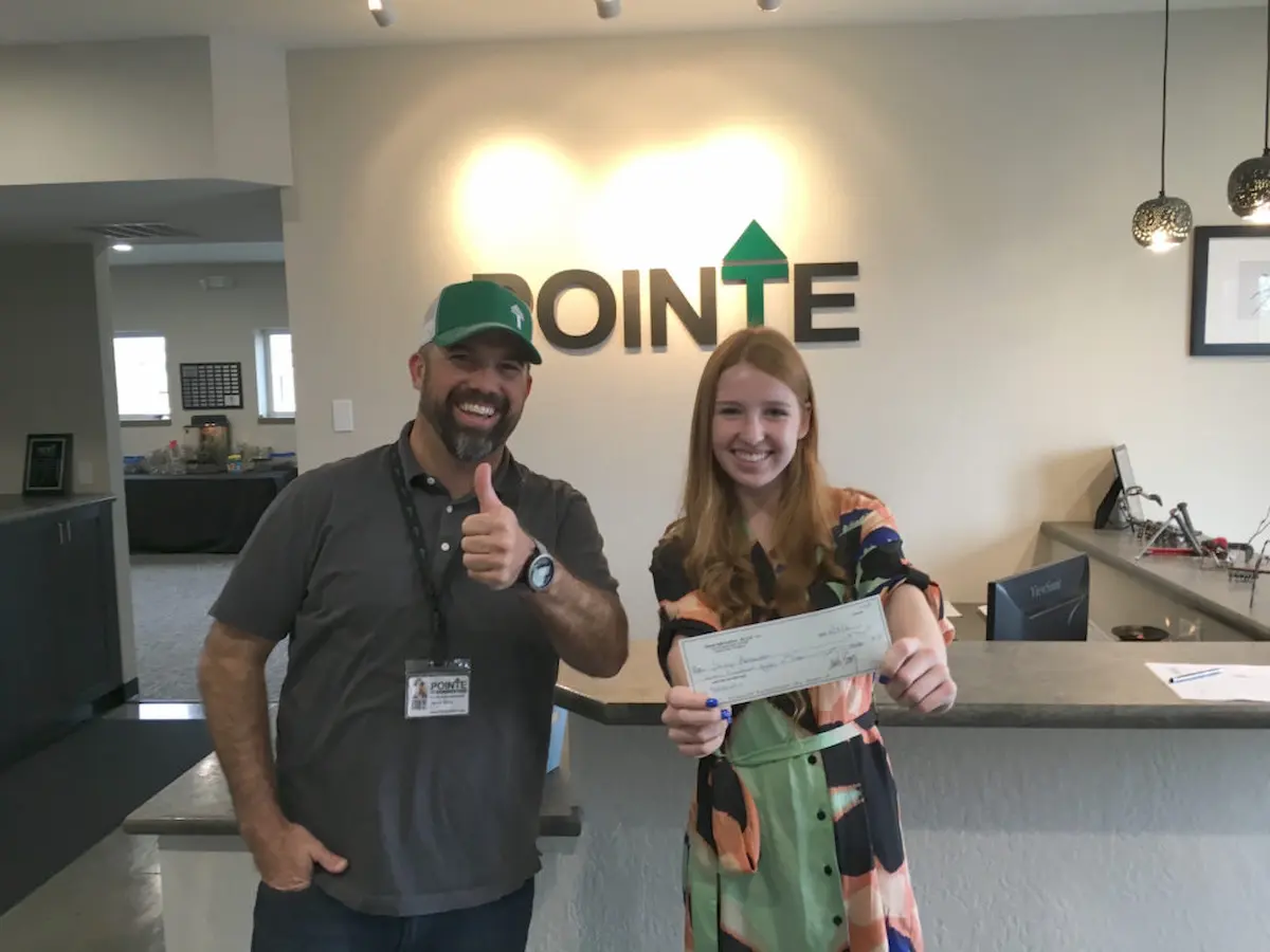 Image of a woman holding a check with a staff member inside a Pointe office reception area