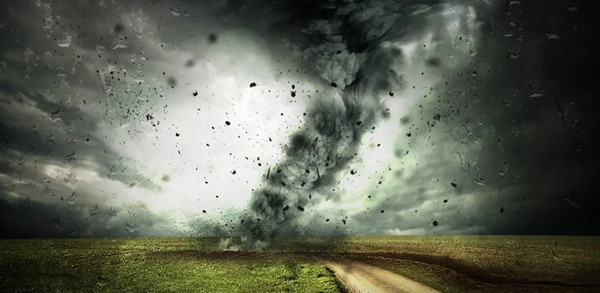Image of a tornado forming over a field with dark storm clouds and debris swirling in the air