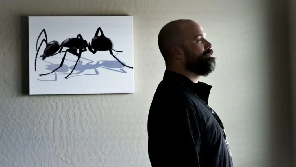 Pointe Pest Control team member standing indoors beside wall art of an ant, representing professional pest control services