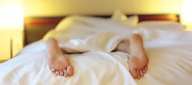 Person sleeping comfortably in bed with feet sticking out from under the blanket in a bedroom setting