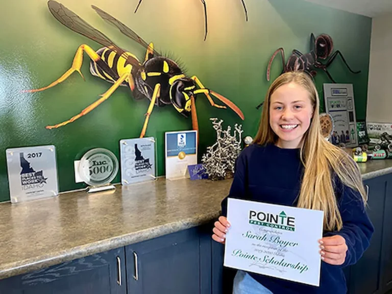 Image of Sara Boyer holding a Pointe scholarship certificate inside an office with pest-themed wall art