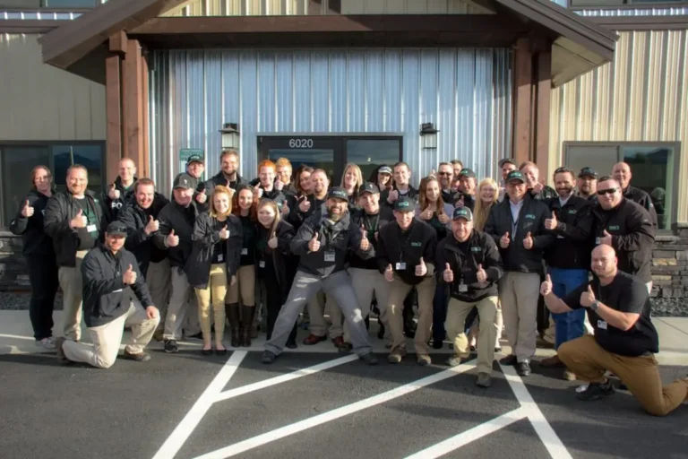 Image of a large team posing together outside an office building giving thumbs up
