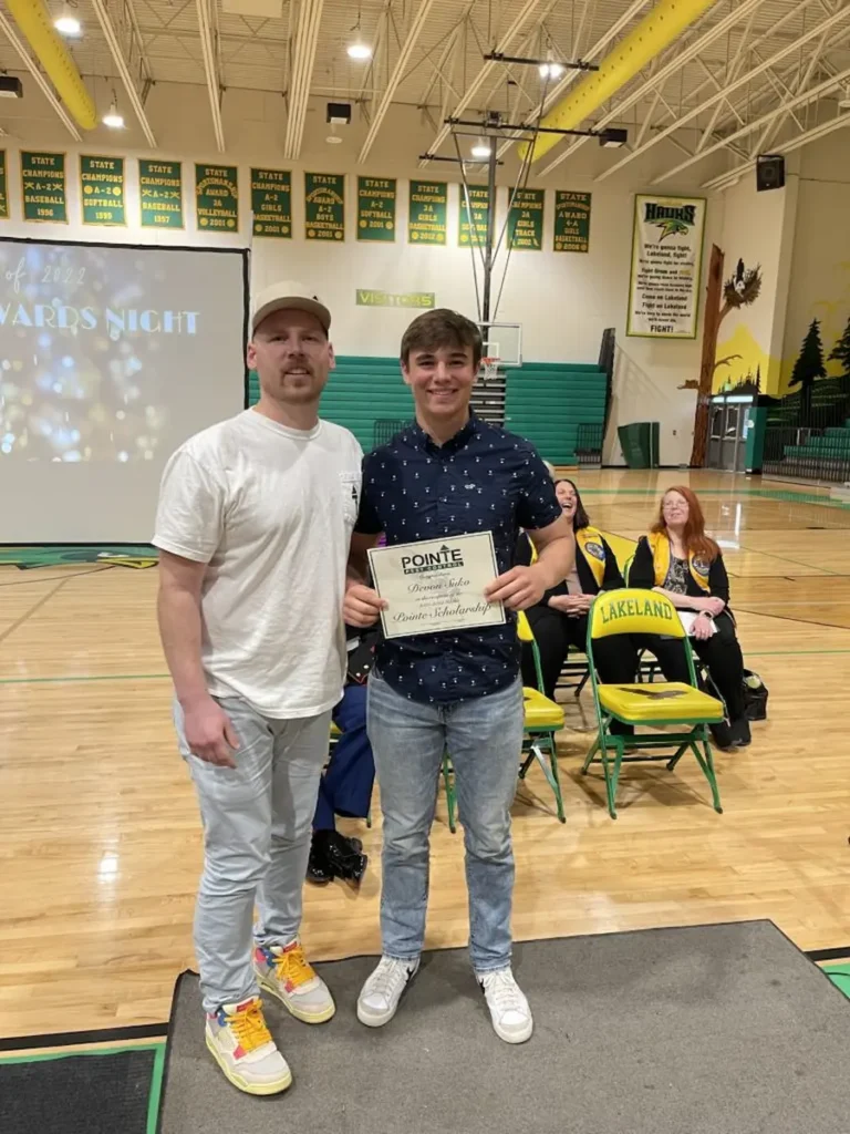 Image of a student holding a scholarship certificate while standing in a school gym with another person during an awards event