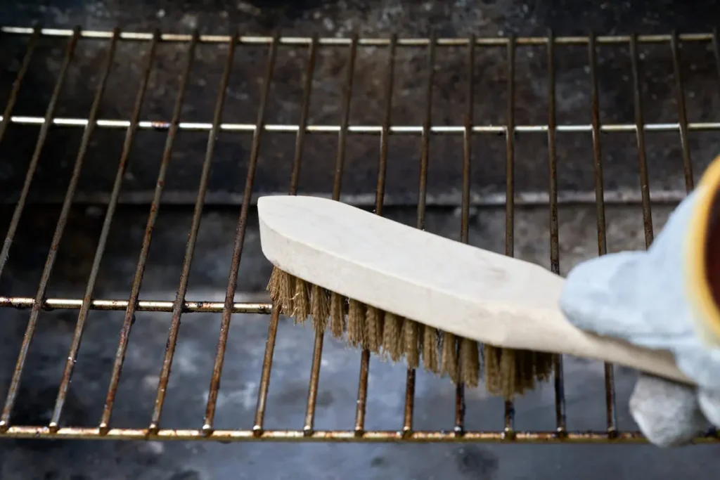 Image of a person cleaning a barbecue grill with a wire brush