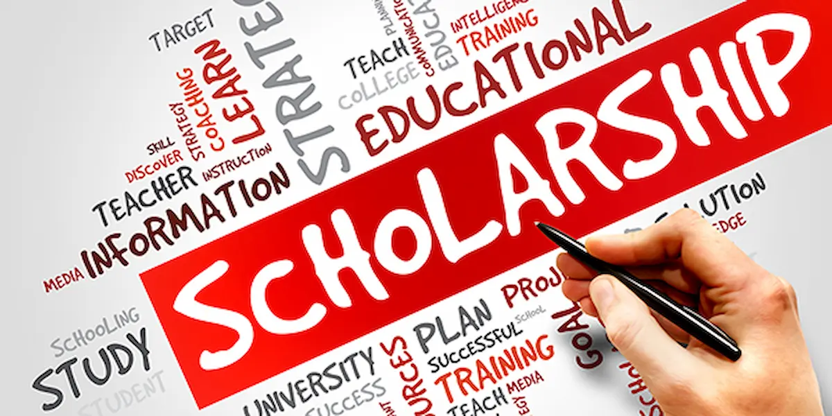 Hand writing the word scholarship over an educational word cloud background featuring terms like learning, training, and study